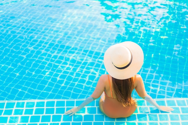 La bella giovane donna asiatica del ritratto si rilassa il tempo libero di sorriso intorno alla piscina all'aperto con la vista dell'oceano del mare