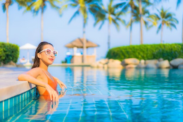 La bella giovane donna asiatica del ritratto si rilassa il tempo libero di sorriso intorno alla piscina all'aperto con la vista dell'oceano del mare