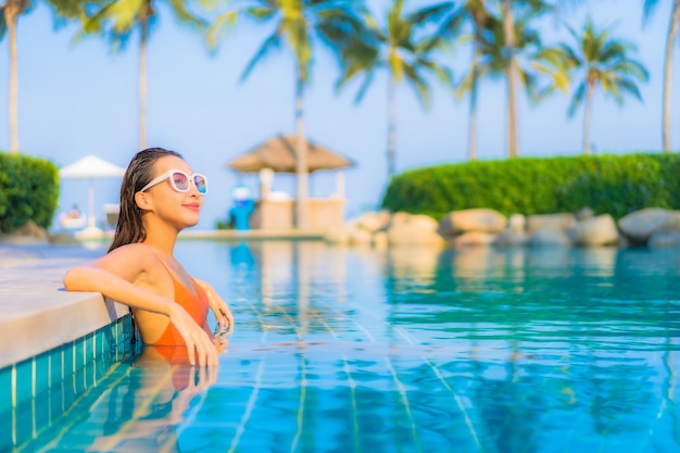 La bella giovane donna asiatica del ritratto si rilassa il tempo libero di sorriso intorno alla piscina all'aperto con la vista dell'oceano del mare