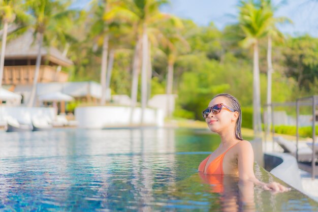 La bella giovane donna asiatica del ritratto si rilassa il tempo libero di sorriso intorno alla piscina all'aperto nell'hotel della località di soggiorno con la vista dell'oceano del mare