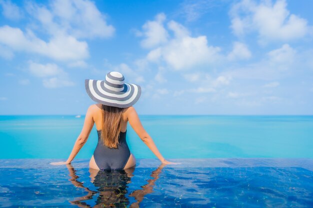 La bella giovane donna asiatica del ritratto si rilassa il tempo libero di sorriso intorno alla piscina all'aperto nell'hotel della località di soggiorno con la vista dell'oceano del mare