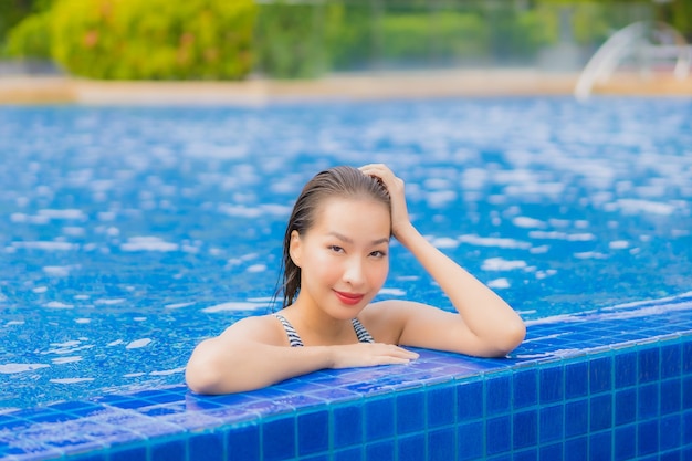 La bella giovane donna asiatica del ritratto si rilassa il tempo libero di sorriso intorno alla piscina all'aperto nella località di soggiorno dell'hotel sul viaggio di vacanza