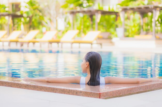 La bella giovane donna asiatica del ritratto si rilassa il tempo libero di sorriso intorno alla piscina all'aperto nella località di soggiorno dell'hotel sul viaggio di vacanza