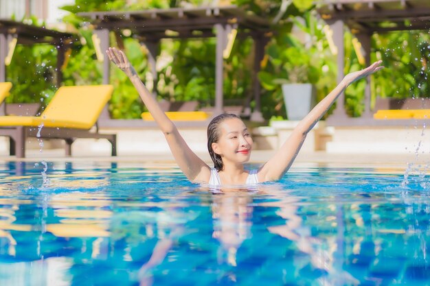 La bella giovane donna asiatica del ritratto si rilassa il tempo libero di sorriso intorno alla piscina all'aperto nella località di soggiorno dell'hotel sul viaggio di vacanza