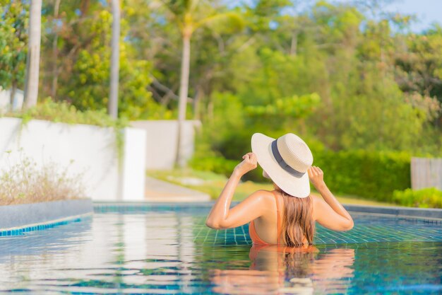 La bella giovane donna asiatica del ritratto si rilassa il tempo libero di sorriso intorno alla piscina all'aperto nella località di soggiorno dell'hotel sulla vacanza di viaggio