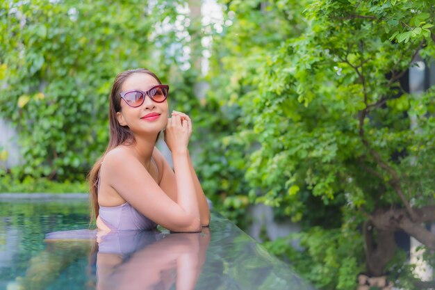 La bella giovane donna asiatica del ritratto si rilassa il tempo libero di sorriso intorno alla piscina all'aperto nella località di soggiorno dell'hotel