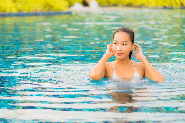 La bella giovane donna asiatica del ritratto si rilassa il tempo libero di sorriso intorno alla piscina all'aperto quasi il mare