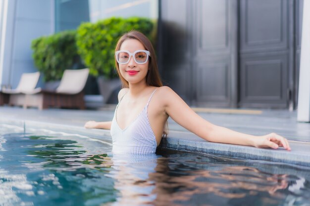 La bella giovane donna asiatica del ritratto si rilassa il tempo libero di sorriso intorno alla piscina all'aperto