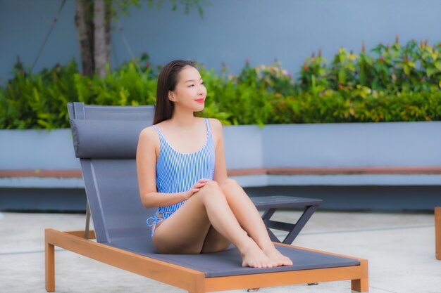 La bella giovane donna asiatica del ritratto si rilassa il tempo libero di sorriso intorno alla piscina all'aperto