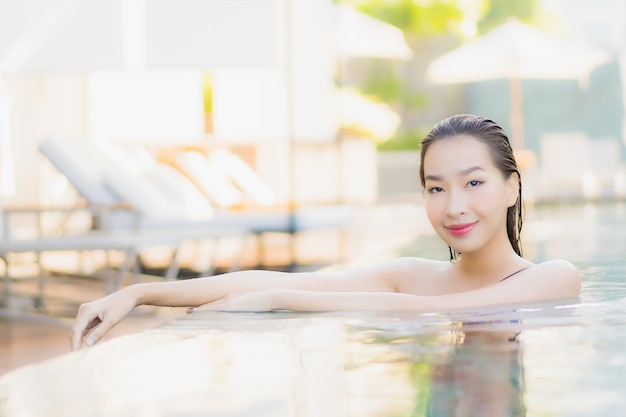 La bella giovane donna asiatica del ritratto si rilassa il tempo libero di sorriso intorno alla piscina all'aperto