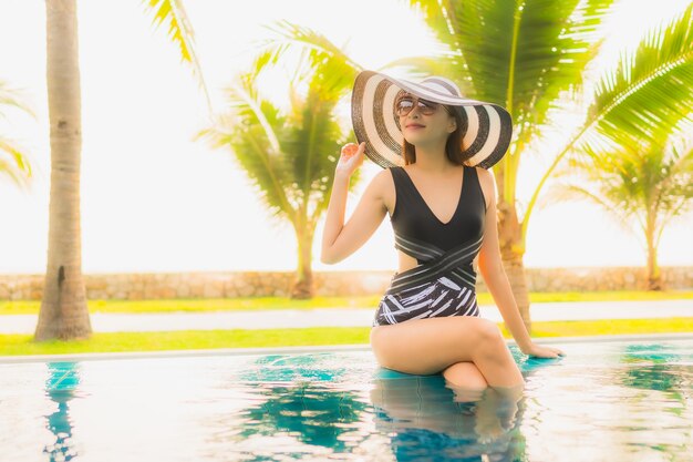 La bella giovane donna asiatica del ritratto si rilassa intorno alla piscina all'aperto nella località di soggiorno dell'hotel con la palma al tramonto o all'alba