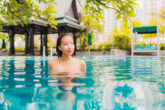 La bella giovane donna asiatica del ritratto si rilassa lo svago felice di sorriso intorno alla piscina all'aperto
