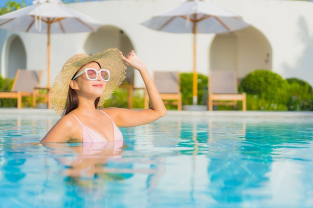 La bella giovane donna asiatica del ritratto si rilassa lo svago intorno alla piscina all'aperto con il mare