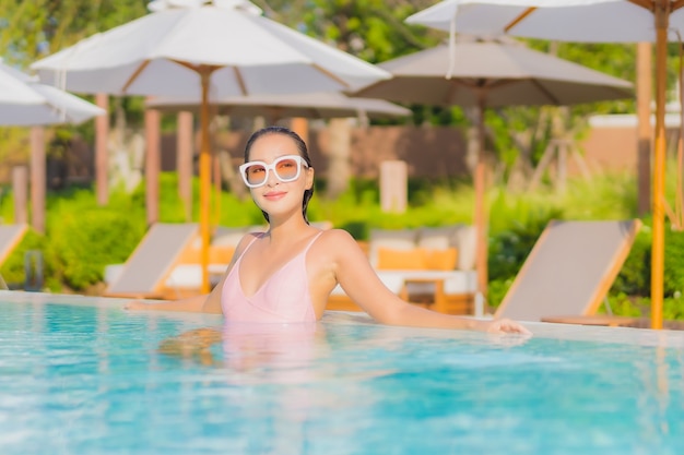 La bella giovane donna asiatica del ritratto si rilassa lo svago intorno alla piscina all'aperto con il mare