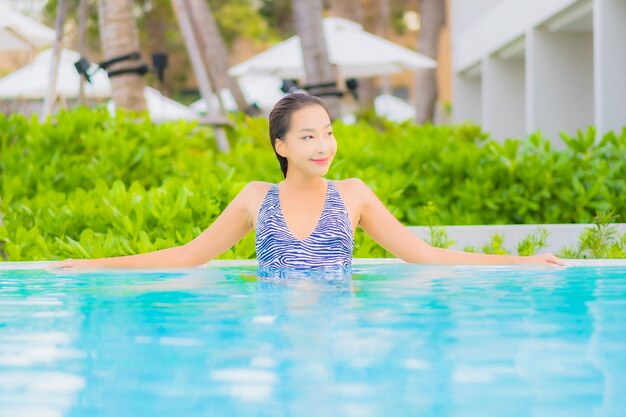 La bella giovane donna asiatica del ritratto si rilassa lo svago intorno alla piscina all'aperto con la spiaggia dell'oceano del mare