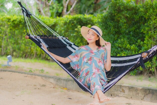 La bella giovane donna asiatica del ritratto si siede sull'oscillazione dell'amaca intorno all'oceano del mare della spiaggia in vacanza di festa