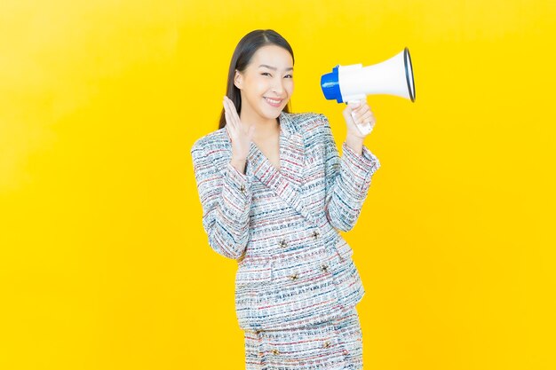 La bella giovane donna asiatica del ritratto sorride con il megafono sulla parete di colore