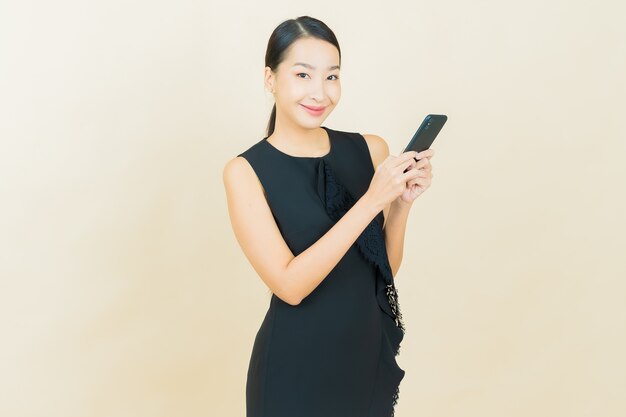 La bella giovane donna asiatica del ritratto sorride con il telefono cellulare astuto sulla parete di colore