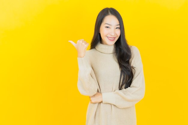 La bella giovane donna asiatica del ritratto sorride con l'azione sulla parete gialla