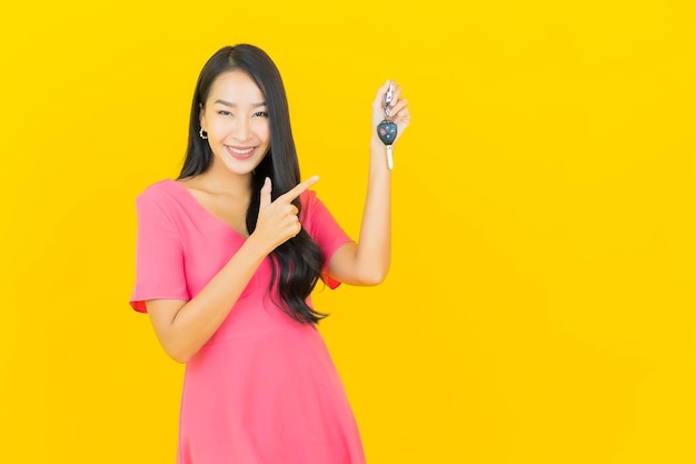La bella giovane donna asiatica del ritratto sorride con la chiave dell'automobile sulla parete gialla