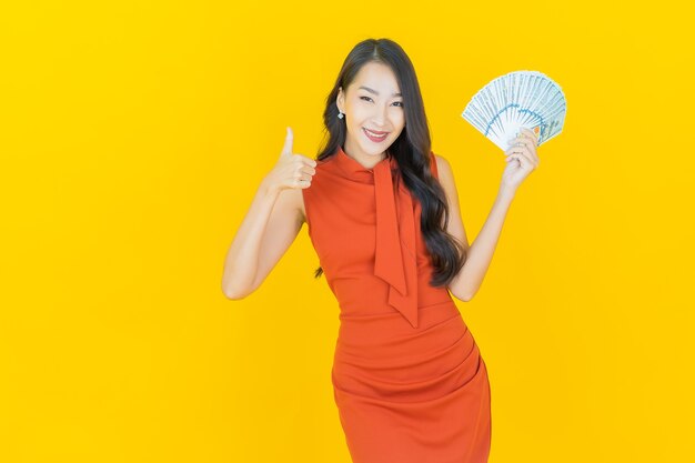 La bella giovane donna asiatica del ritratto sorride con molti contanti e soldi su yellow