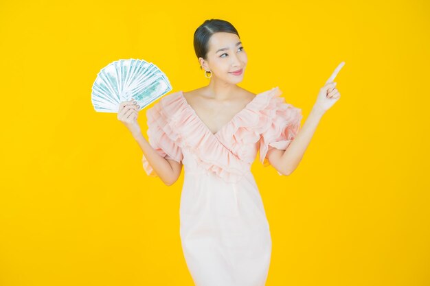 La bella giovane donna asiatica del ritratto sorride con molti contanti e soldi su yellow