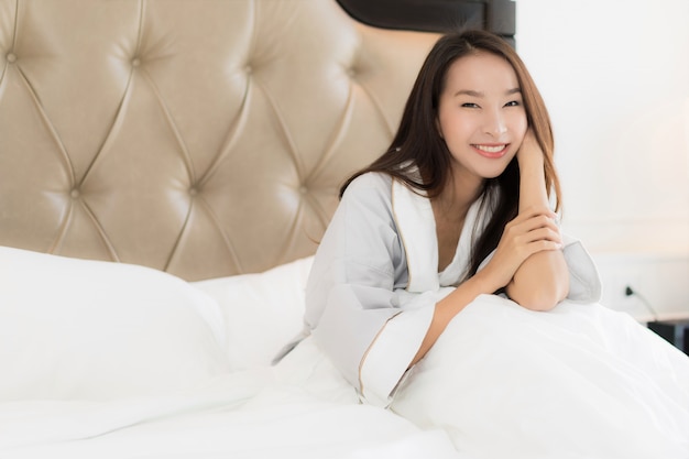 La bella giovane donna asiatica del ritratto sveglia con felice e sorride sul letto nell&#39;interno della camera da letto