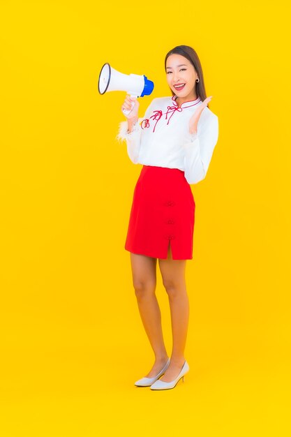 La bella giovane donna asiatica del ritratto usa il megafono su yellow