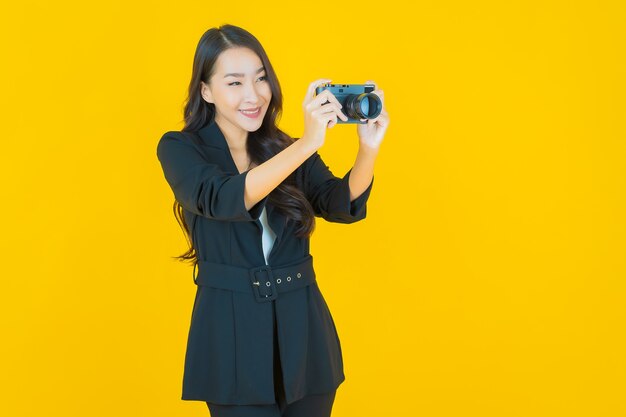 La bella giovane donna asiatica del ritratto usa la macchina fotografica su yellow