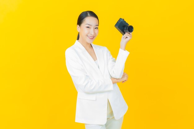 La bella giovane donna asiatica del ritratto usa la macchina fotografica sulla parete di colore