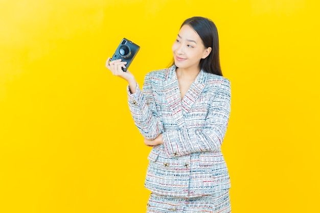 La bella giovane donna asiatica del ritratto usa la macchina fotografica sulla parete di colore