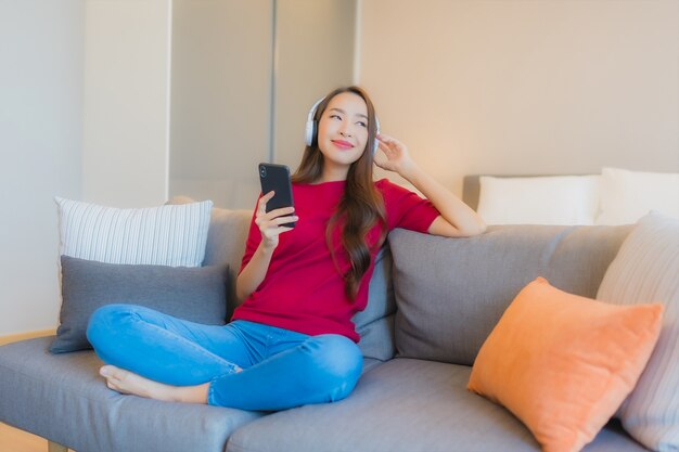 La bella giovane donna asiatica del ritratto utilizza il telefono cellulare astuto con la cuffia per ascoltare la musica