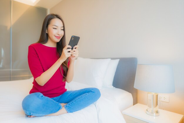 La bella giovane donna asiatica del ritratto utilizza il telefono cellulare astuto sul letto