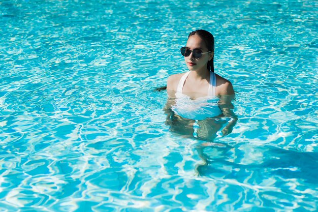 La bella giovane donna asiatica felice e sorride nella piscina per si rilassa il viaggio e la vacanza