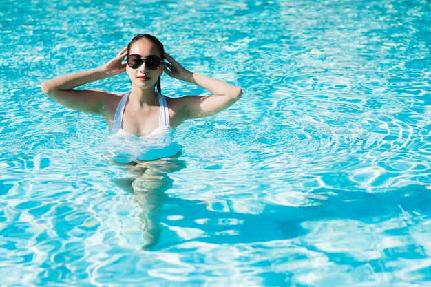 La bella giovane donna asiatica felice e sorride nella piscina per si rilassa il viaggio e la vacanza