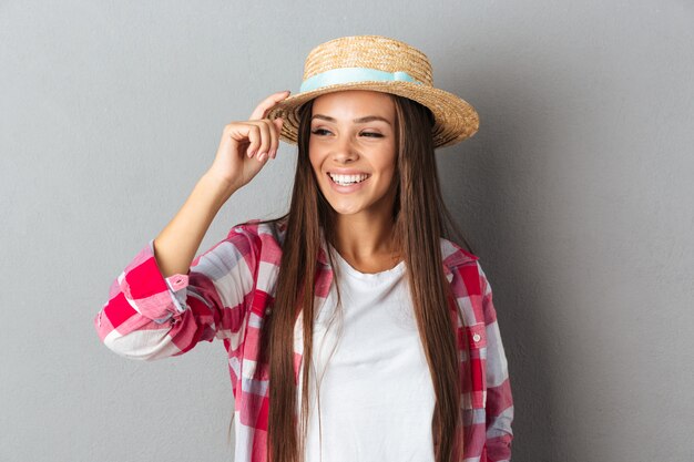 La bella giovane donna caucasica ride e tocca il suo cappello di paglia