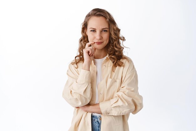 La bella giovane donna con la faccia determinata e premurosa che sembra pronta e seria alla macchina fotografica ha preso la sua decisione in piedi fiducioso su sfondo bianco