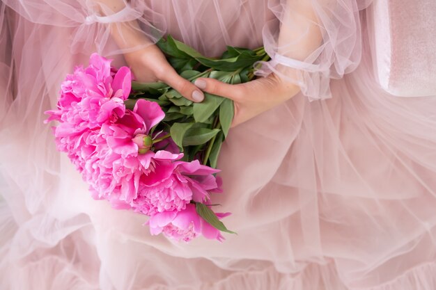 La bella giovane donna in vestito rosa che tiene la peonia fiorisce il mazzo in sue mani