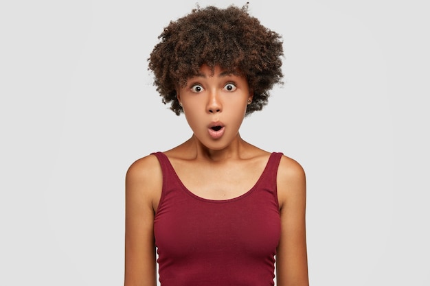 La bella giovane donna stupita ha un taglio di capelli afro, ha una pelle scura e sana