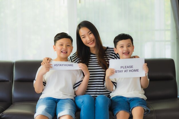 La bella giovane mamma asiatica con i suoi due figli mostra la carta per restare a casa per proteggere il coronavirus