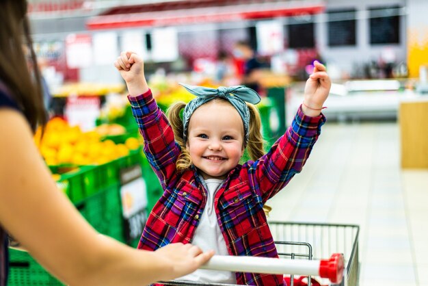 La bella madre porta la sua bambina nel carrello del supermercato