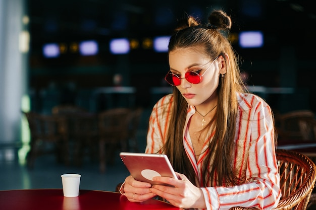 La bella modella in occhiali da sole rossi lavora con il suo tablet seduto al caffè