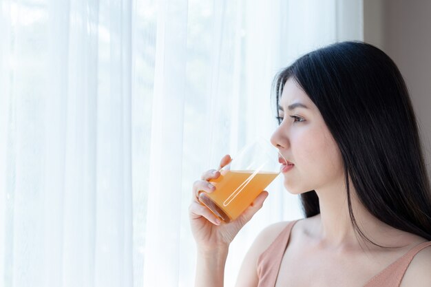 La bella ragazza asiatica di bellezza della ragazza di bellezza ritiene felice il succo d&#39;arancia bevente per buona salute di mattina