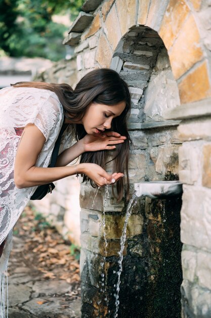 La bella, ragazza beve l'acqua di fonte all'aperto