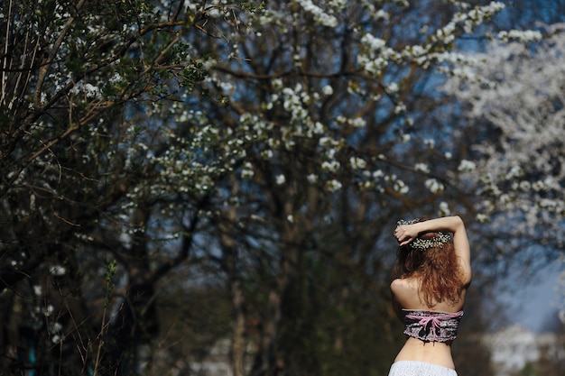 La bella ragazza cammina nel giardino lussureggiante vestita con una ghirlanda