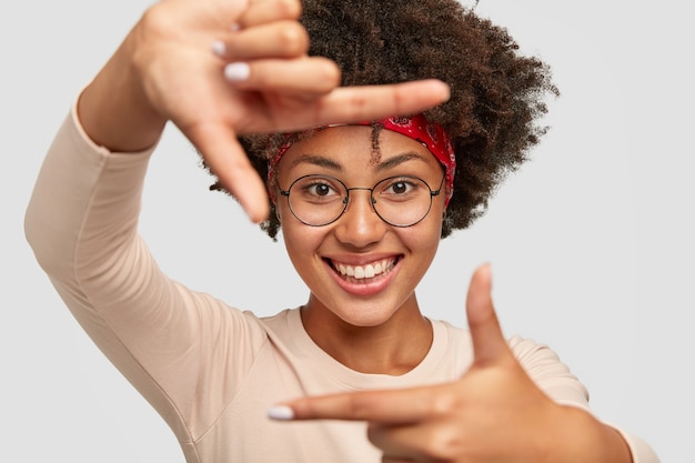 La bella ragazza dalla pelle scura allegra fa la struttura con entrambe le mani ha soddisfatto l'espressione facciale, sorride ampiamente