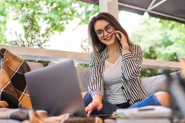 La bella ragazza dello studente impara a casa con il computer portatile e parla dal telefono cellulare.