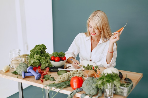 La bella ragazza fa un'insalata. Bionda sportiva in cucina. Ricetta di scrittura della donna in taccuino.