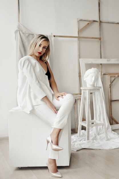 La bella ragazza in un vestito bianco si siede su un cubo bianco in una galleria
