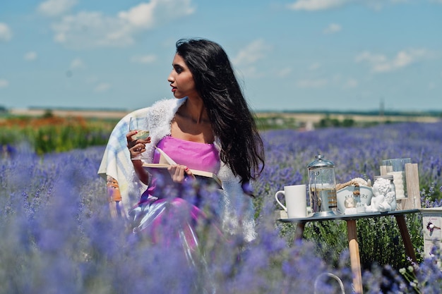 La bella ragazza indiana indossa l'abito tradizionale indiano del saree che si siede nel campo viola della lavanda con l'arredamento